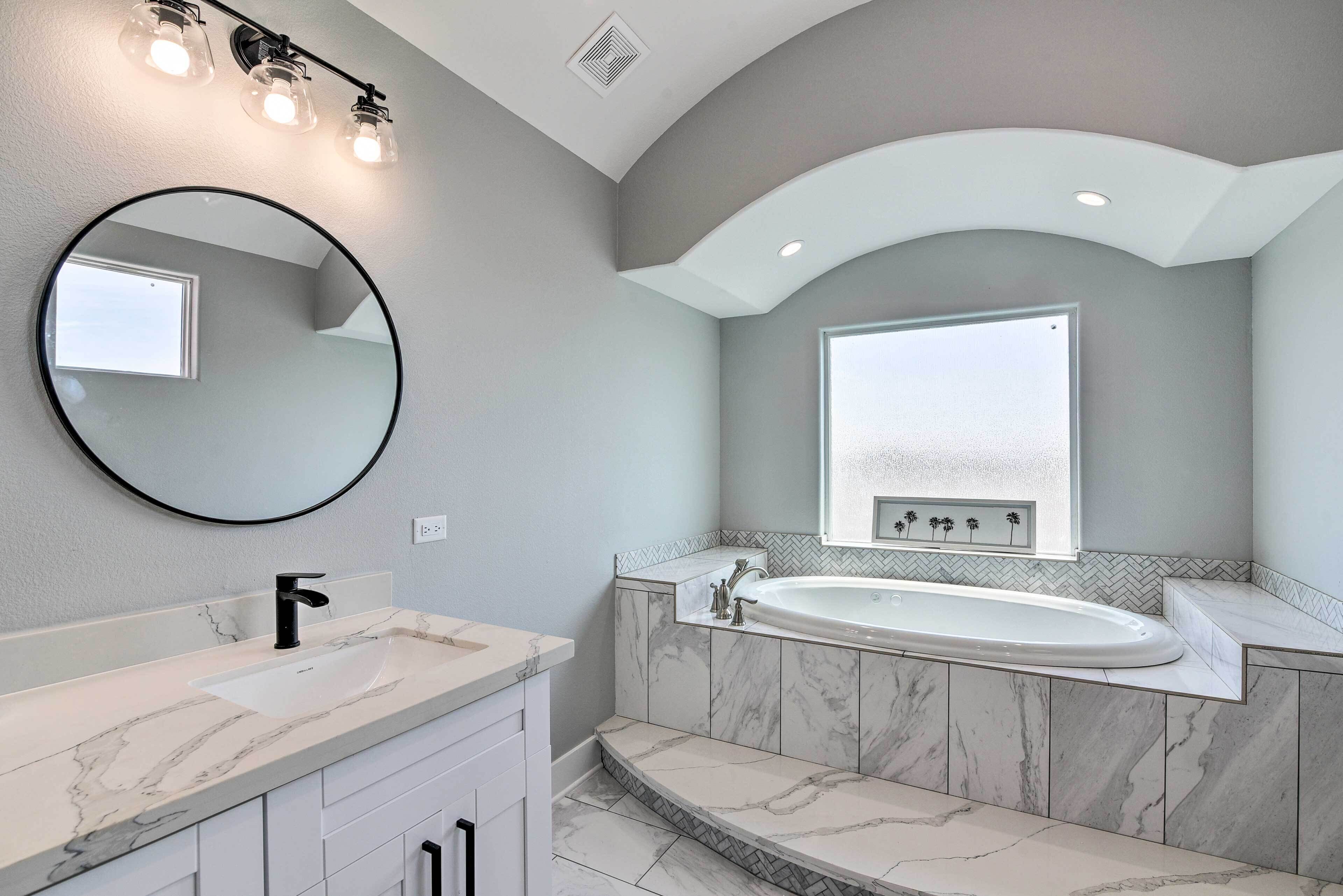 A modern bathroom with a marble sink, a freestanding bathtub, and a large mirror.