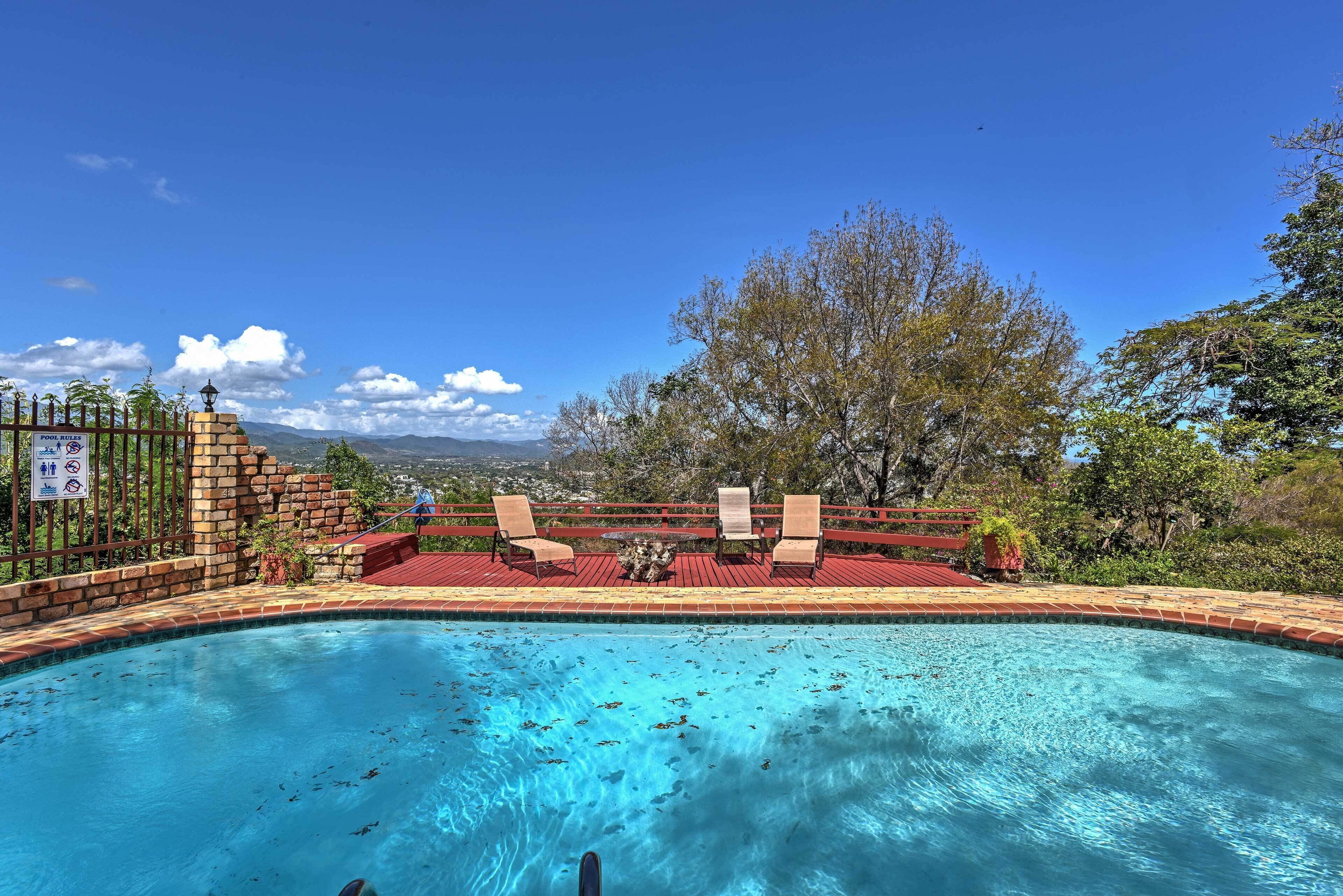 A swimming pool with a view of mountains, a fenced area with chairs, and a sign indicating a no swimming zone.