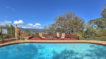 A swimming pool with a view of mountains, a fenced area with chairs, and a sign indicating a no swimming zone.