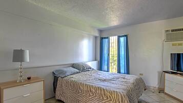 A bedroom with a bed, a bedside table with a lamp, a TV, and a window with curtains.