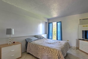 A bedroom with a bed, a bedside table with a lamp, a TV, and a window with curtains.