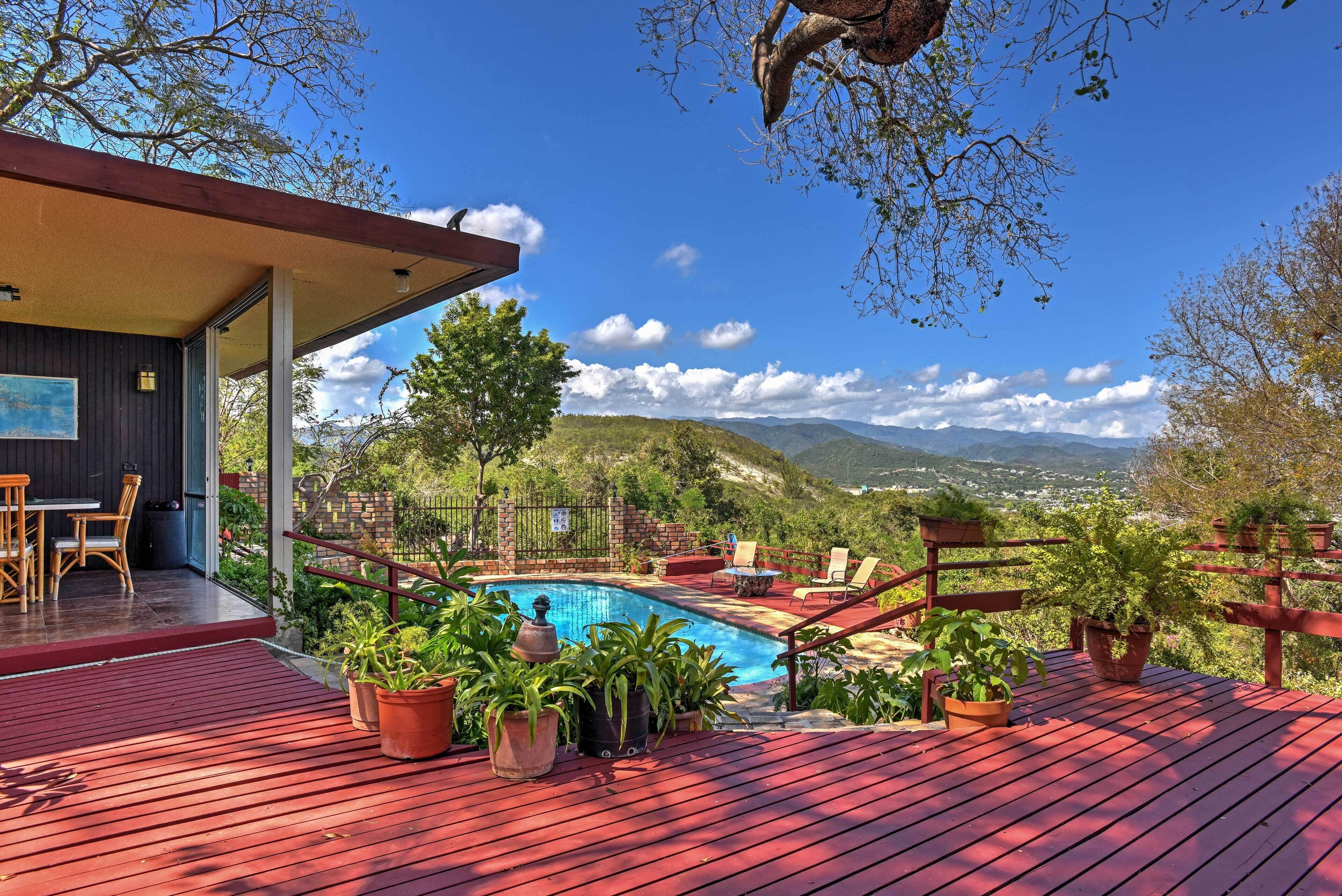 A pool area with a wooden deck, outdoor seating, and potted plants.