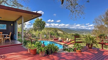 A pool area with a wooden deck, outdoor seating, and potted plants.