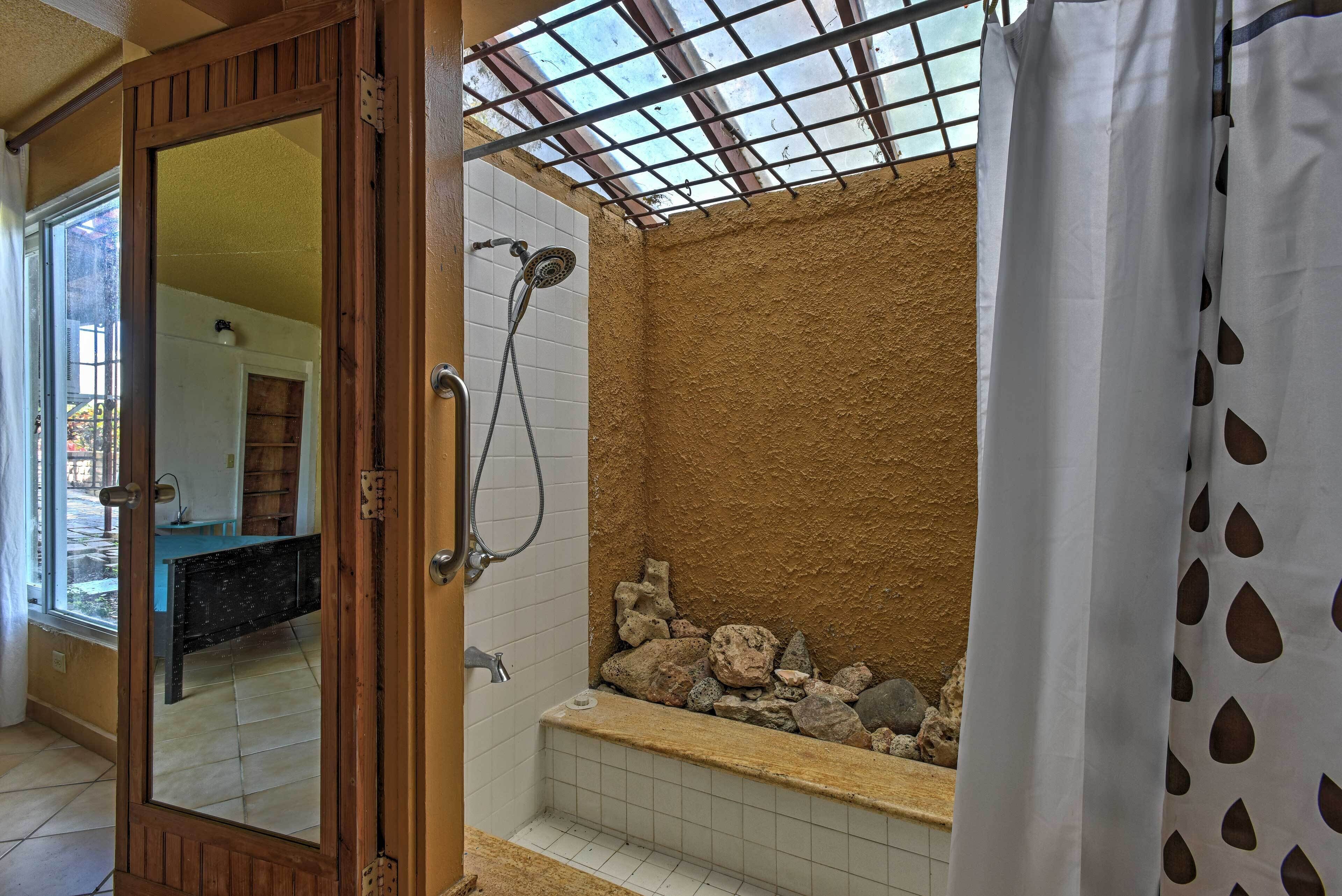 A bathroom with a shower, tiled walls, a bathtub with rocks, and a wooden door.
