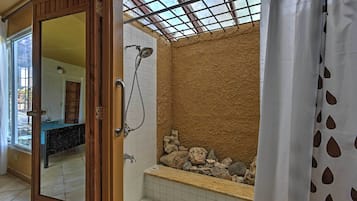 A bathroom with a shower, tiled walls, a bathtub with rocks, and a wooden door.