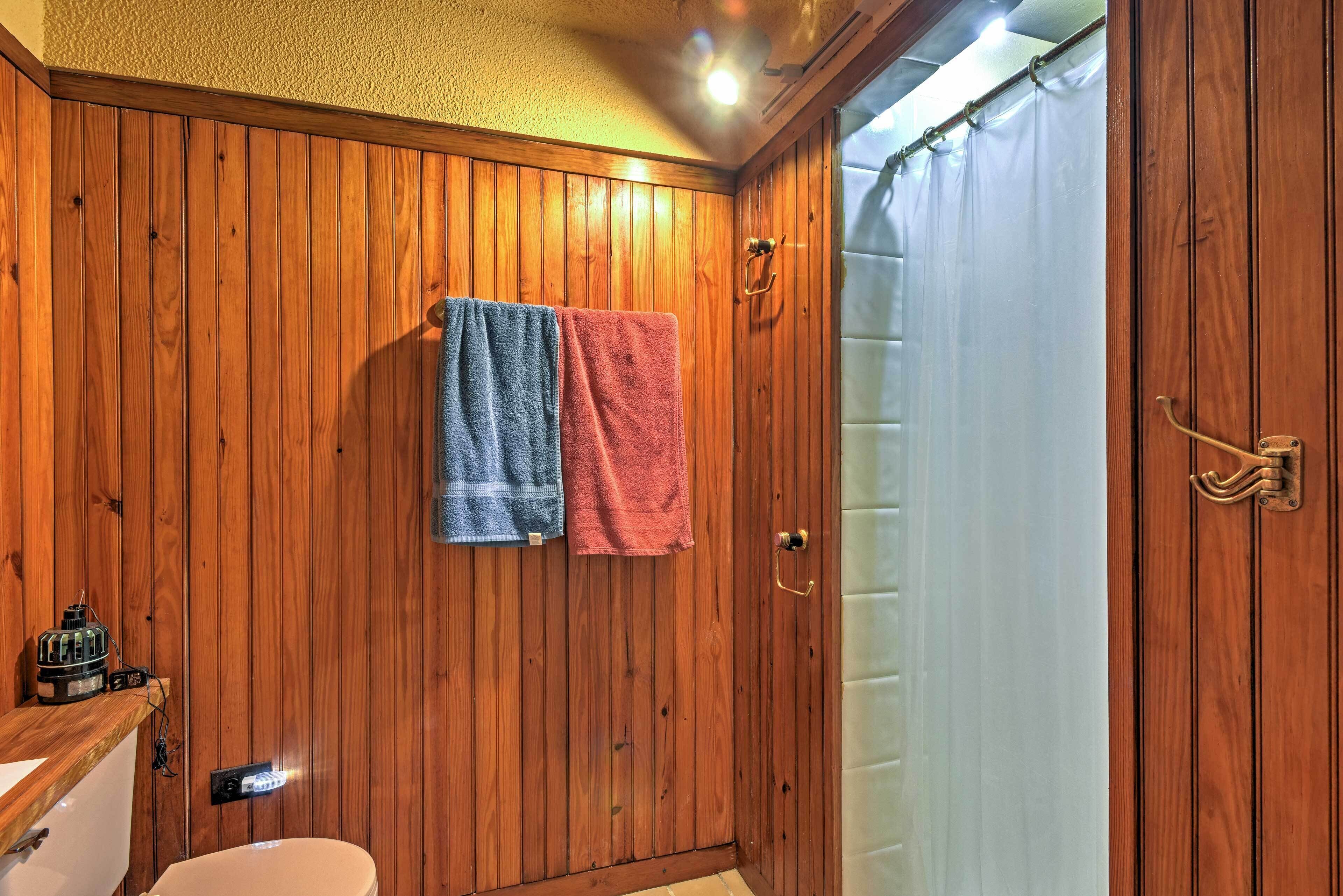 A wooden-paneled bathroom with two towels hanging on the wall, a toilet, and a shower curtain.