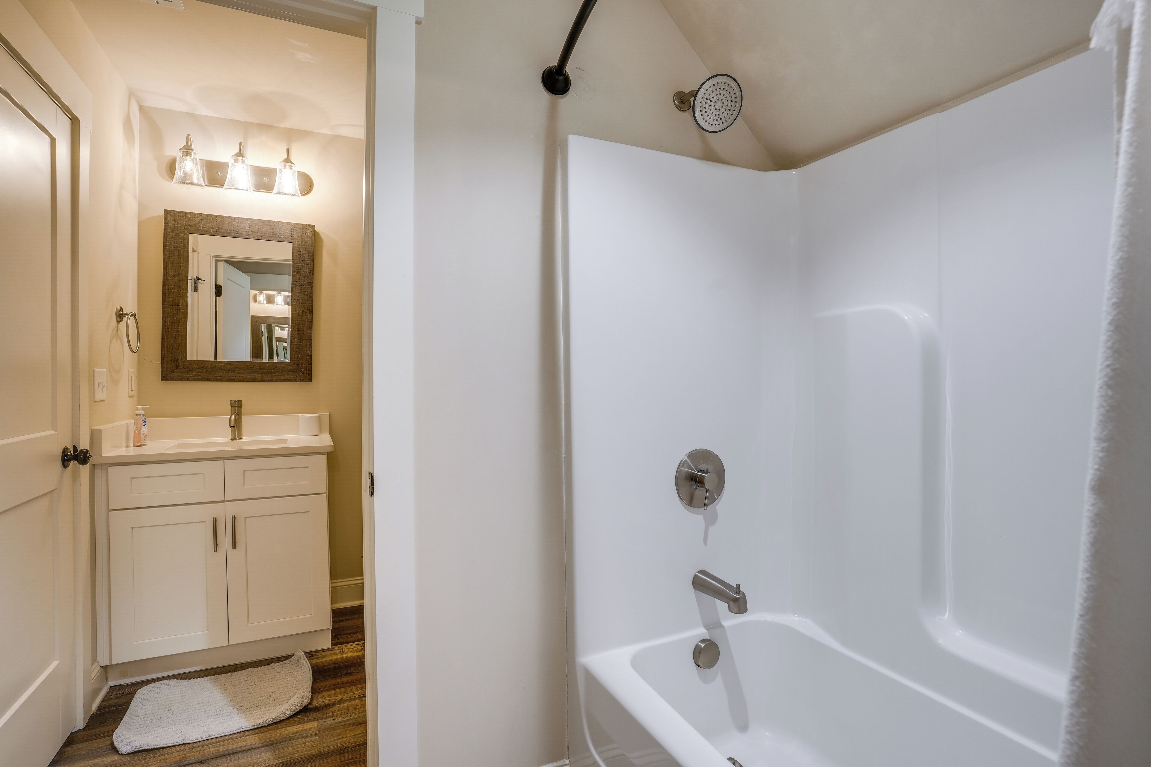 Une salle de bain avec une baignoire blanche, un lavabo avec un miroir au-dessus et une serviette sur le sol.