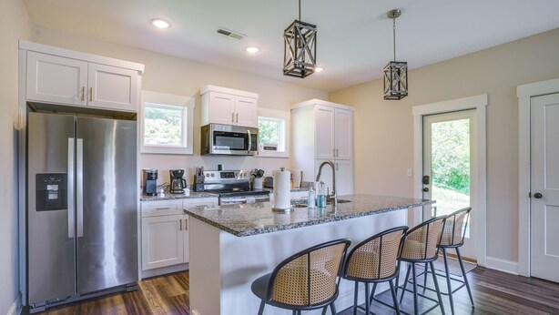 A kitchen with a stainless steel refrigerator, a microwave, and a coffee maker. There are white cabinets and a large island with bar stools.