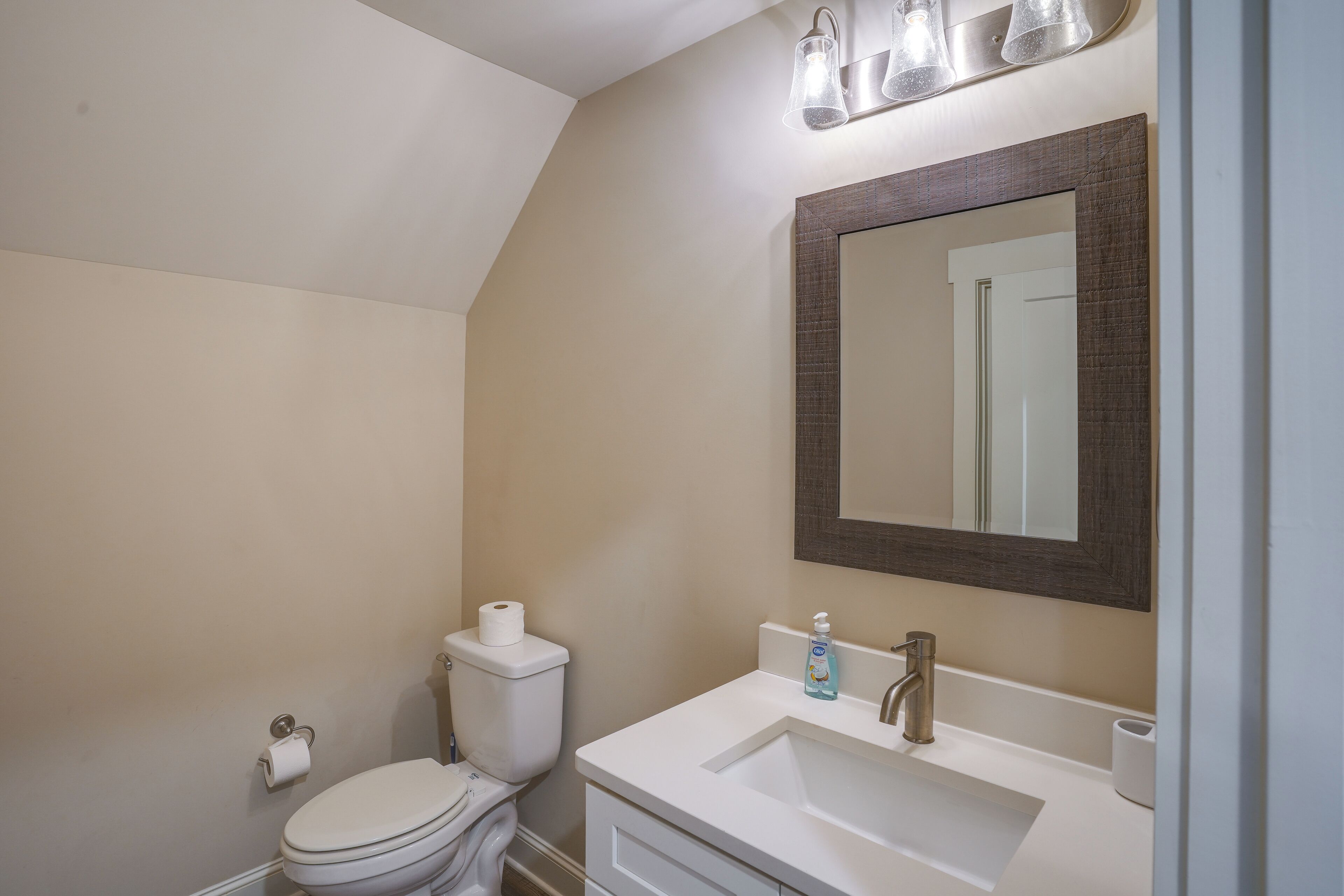A bathroom with a toilet, sink, mirror, and light fixture.