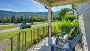 A porch with a view of a road and mountains, a car parked on the street, and a grassy area.
