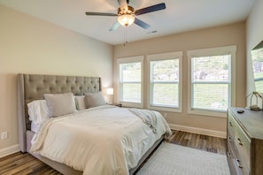 A bedroom with a tufted headboard, a bed with white bedding, a ceiling fan, and three windows with blinds.