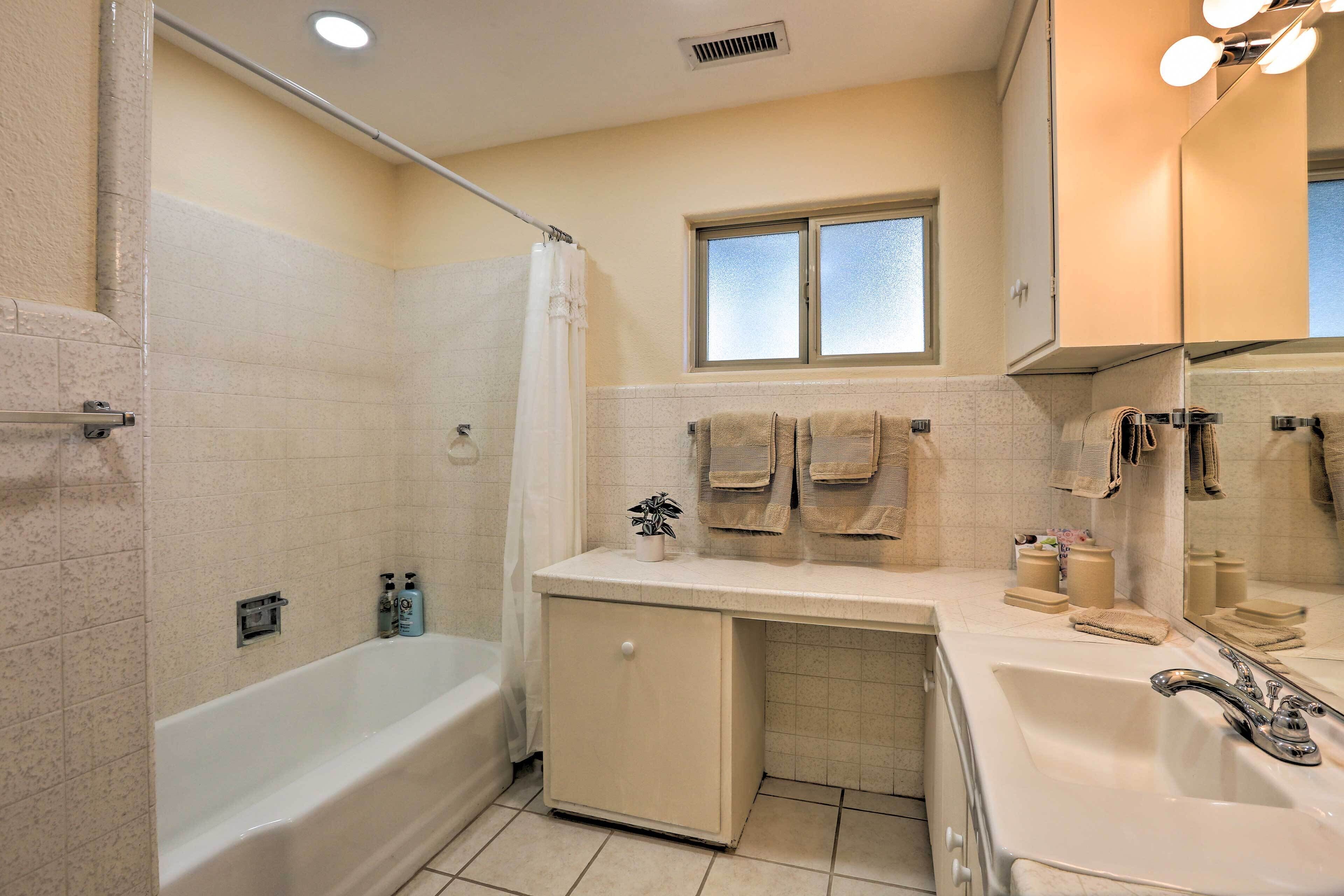 A bathroom with a bathtub, a sink, a window, and a mirror.