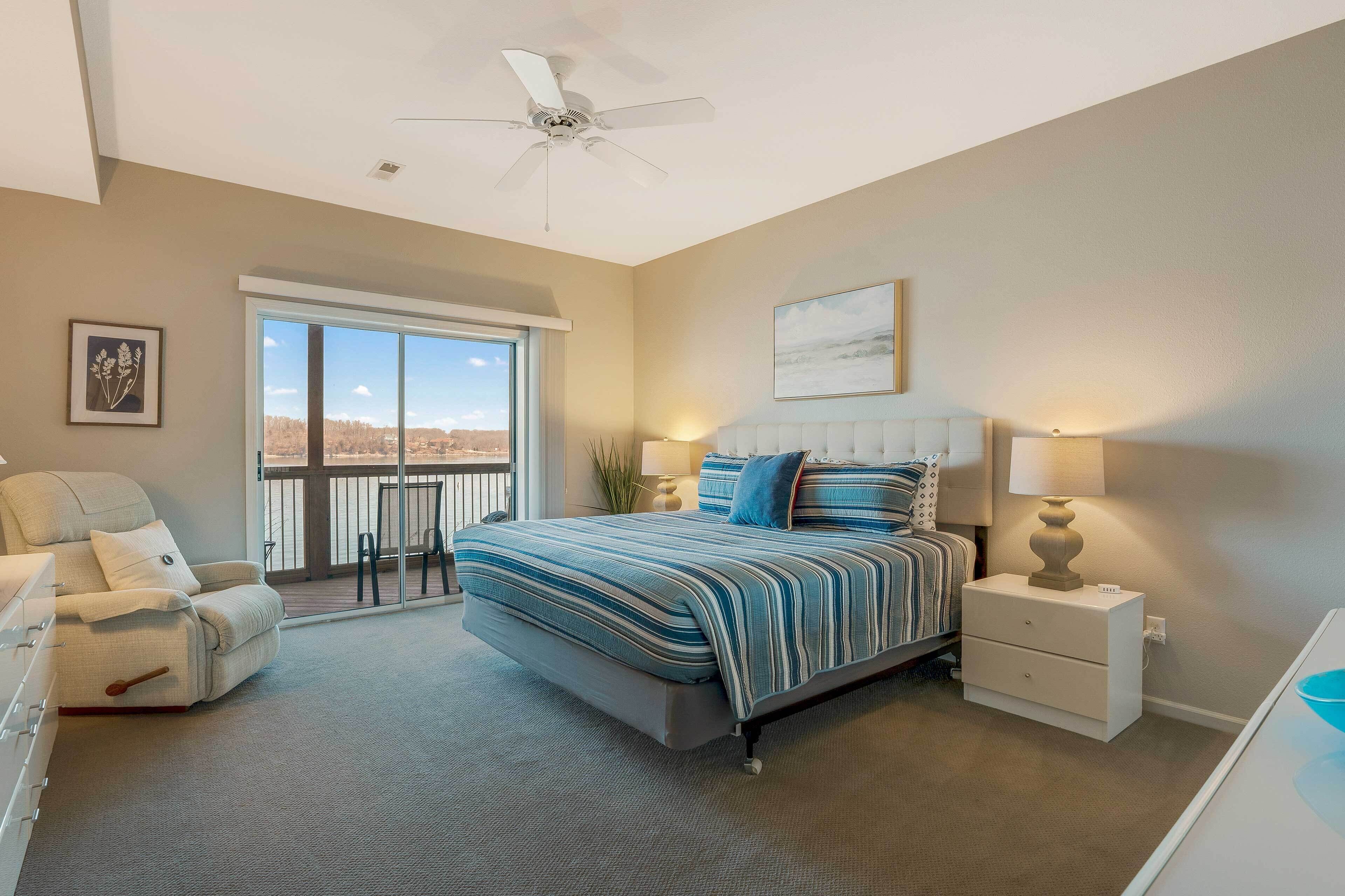 A bedroom with a large bed, a chair, a nightstand, a ceiling fan, and a view through a sliding glass door.
