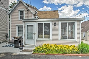 A two-story house with a front porch, a small garden with yellow flowers, and a visible chimney.