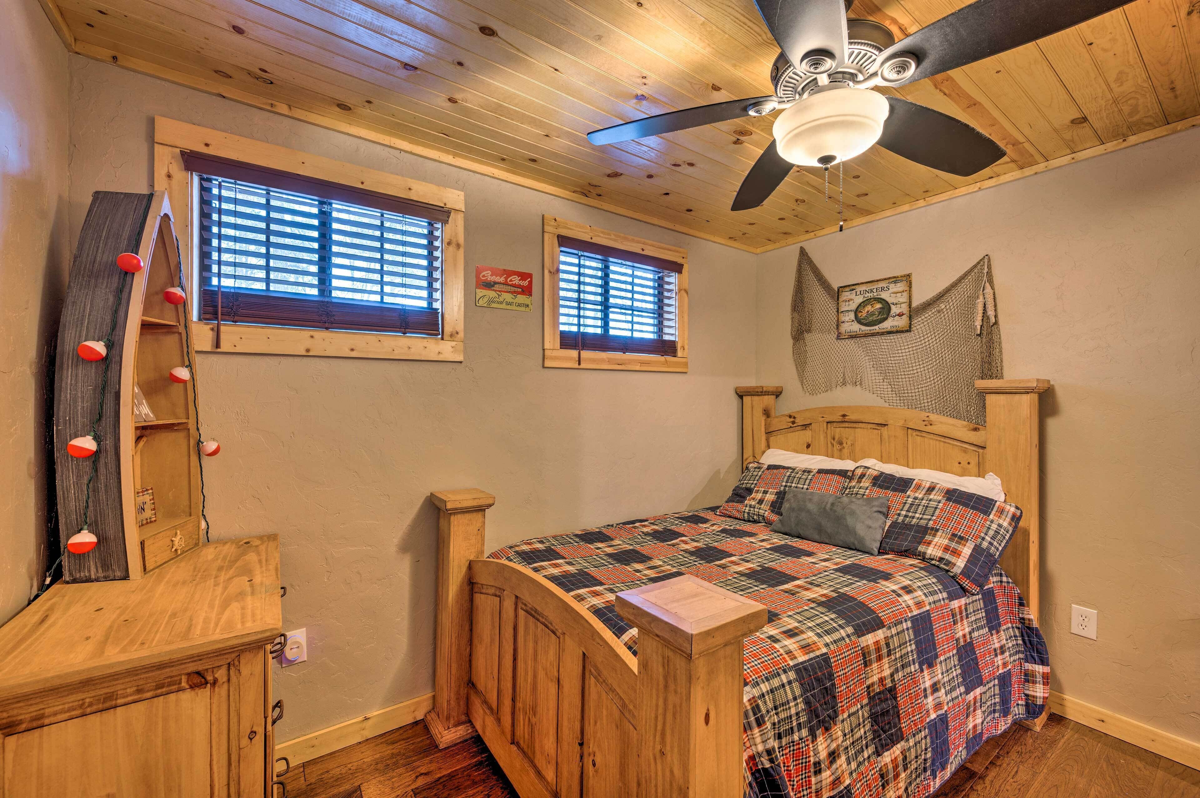 A wooden bed with a plaid bedspread, two windows with blinds, a ceiling fan, and a wooden dresser with a mirror.