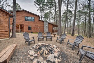 A log cabin with a stone fireplace, outdoor seating, and a forest backdrop.