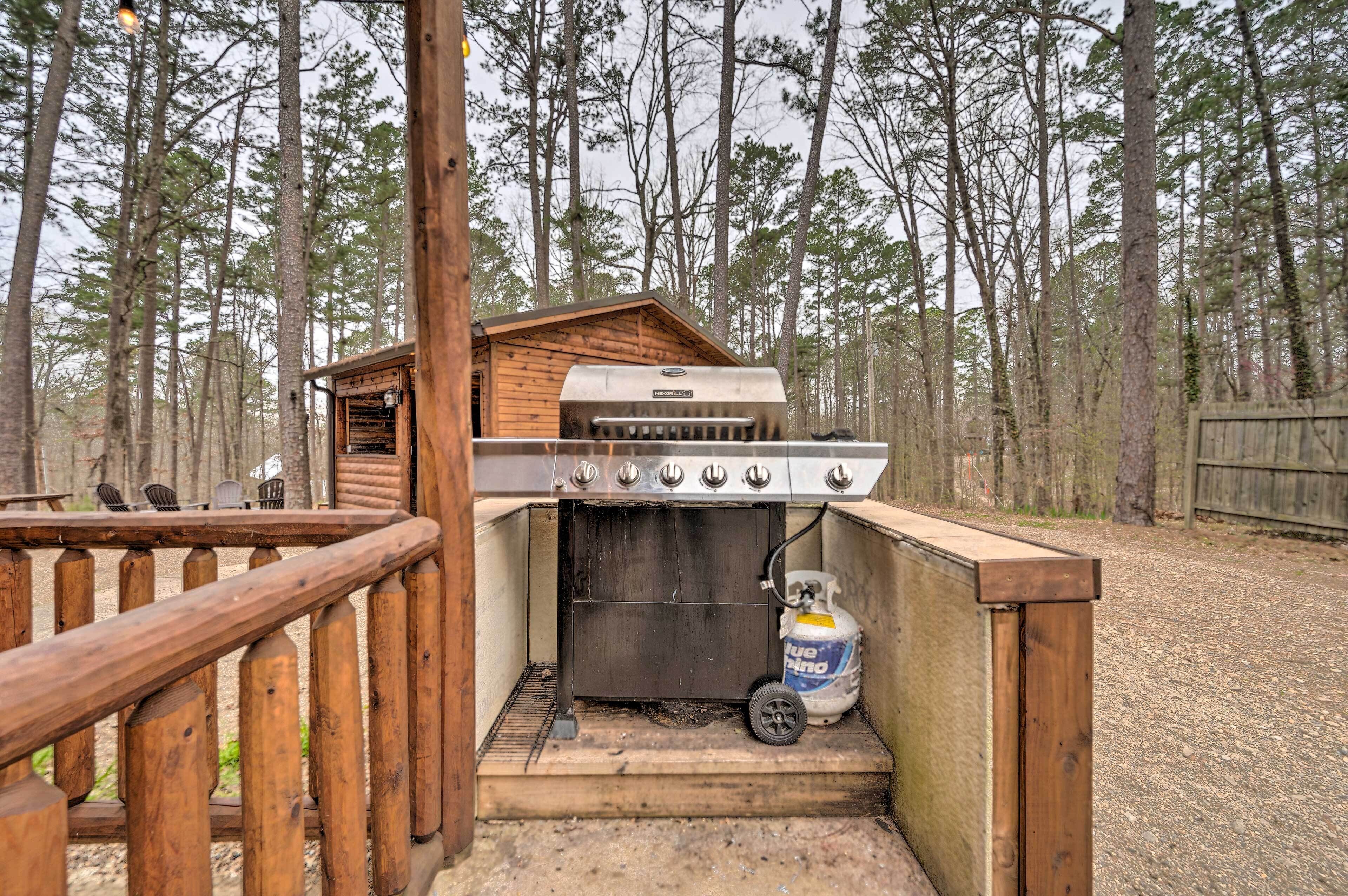 A rustic outdoor grill area with a wooden structure, a gas tank, and a metal grill.