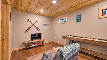 Una habitación acogedora con techo de madera, televisor, mesa de billar y un letrero que dice "GO JUMP IN THE LAKE".