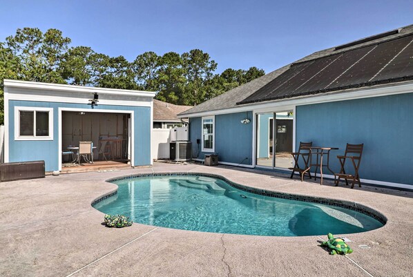 A backyard with a swimming pool, a covered patio, and a blue building with a door.