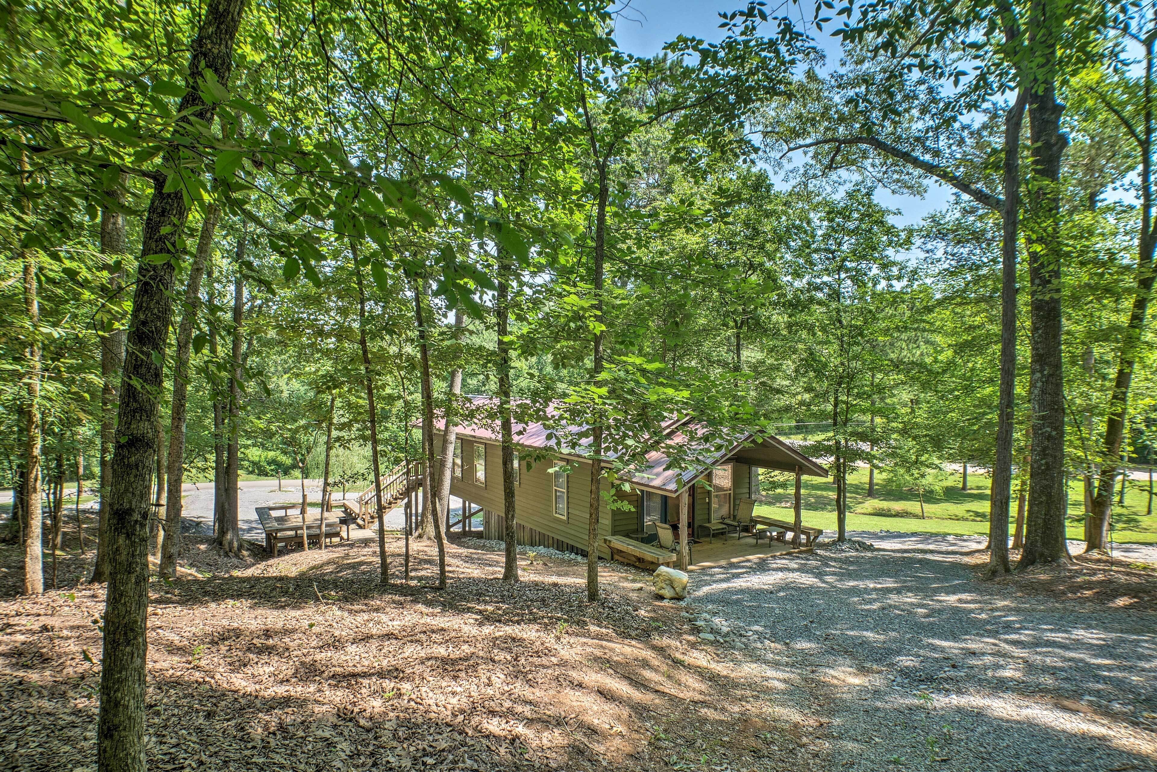 A rustic cabin with a porch, surrounded by trees and a gravel path.