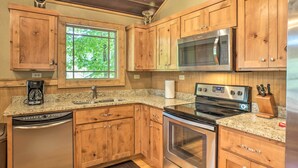 A kitchen with wooden cabinets, a stainless steel microwave, an oven, a dishwasher, and a granite countertop. - The Treehouse at Kudzu Cove Cabins Resort (Guntersville)
