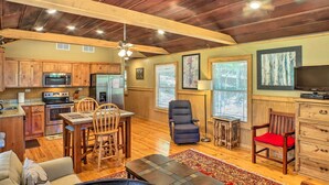 A spacious living area with a wooden ceiling, a dining table with chairs, a sofa, a television, and a kitchen with wooden cabinets and appliances. - The Treehouse at Kudzu Cove Cabins Resort (Guntersville)