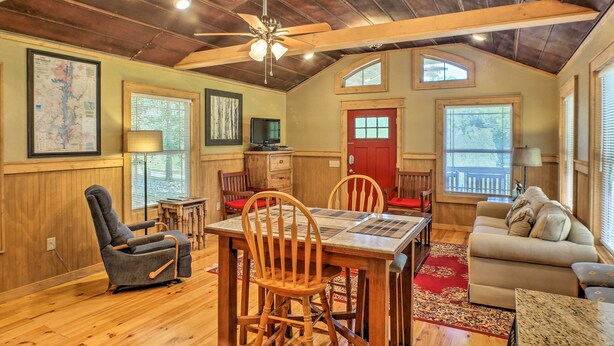 A cozy room with a wooden ceiling, a dining table with chairs, a sofa, and a red door. - The Treehouse at Kudzu Cove Cabins Resort (Guntersville)