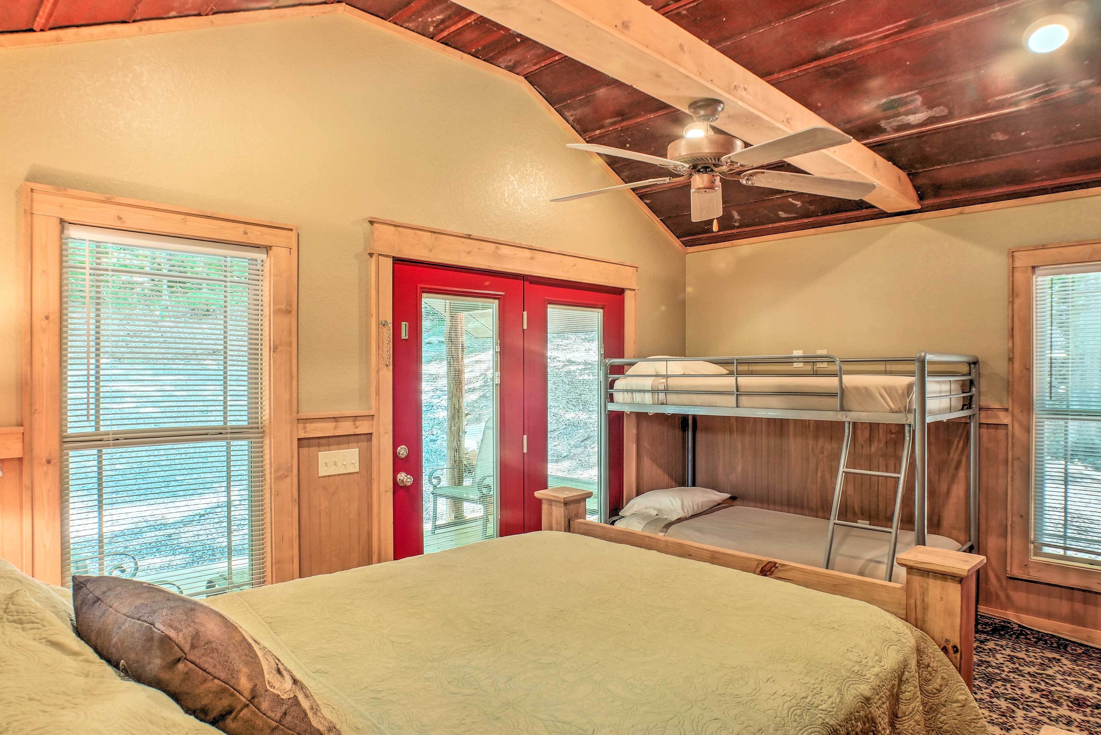 Une chambre avec un lit superposé, un ventilateur de plafond, des murs en bois et une porte rouge.