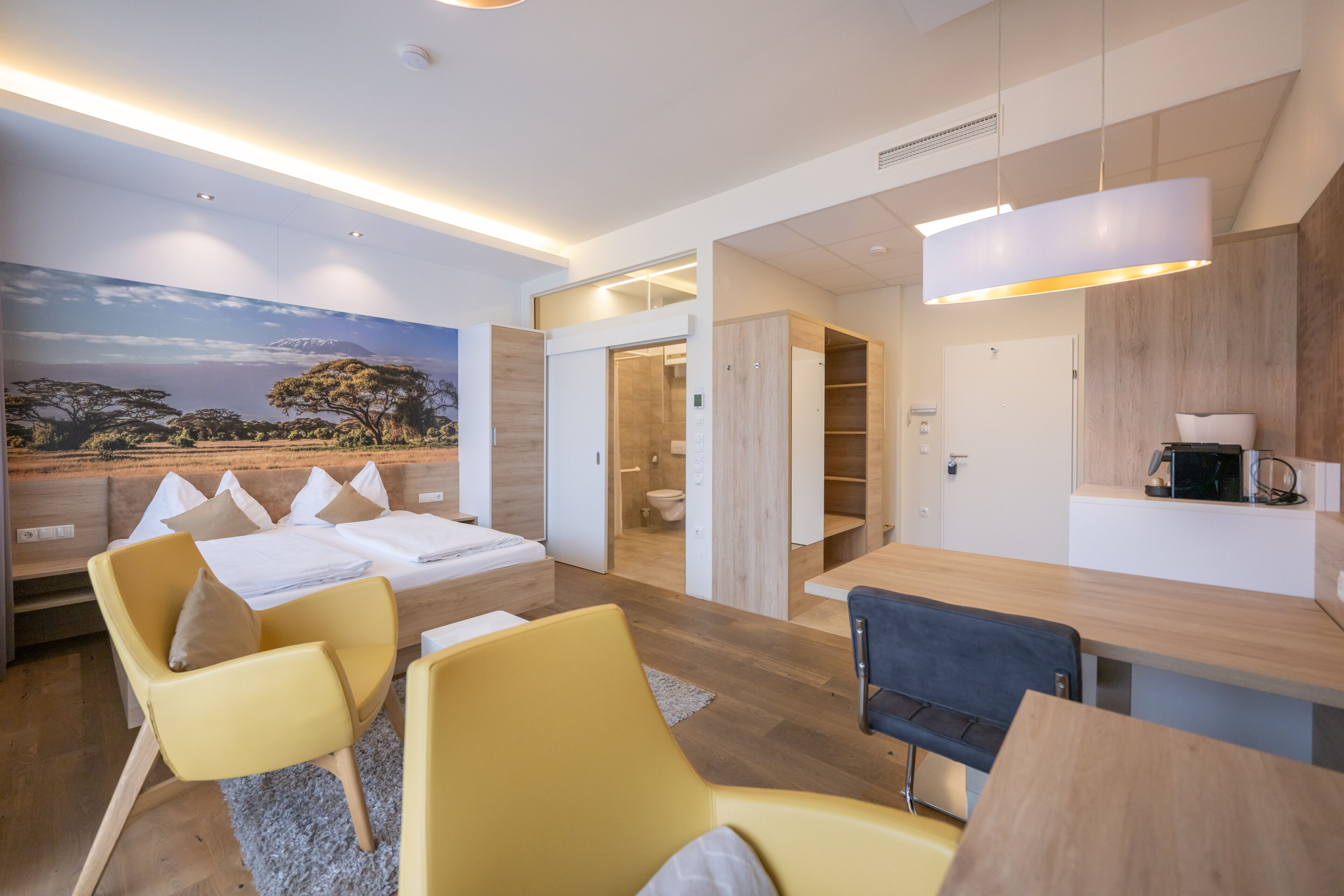 Una camera d'albergo moderna con un letto, sedie gialle, un tavolo da pranzo e un angolo cottura.