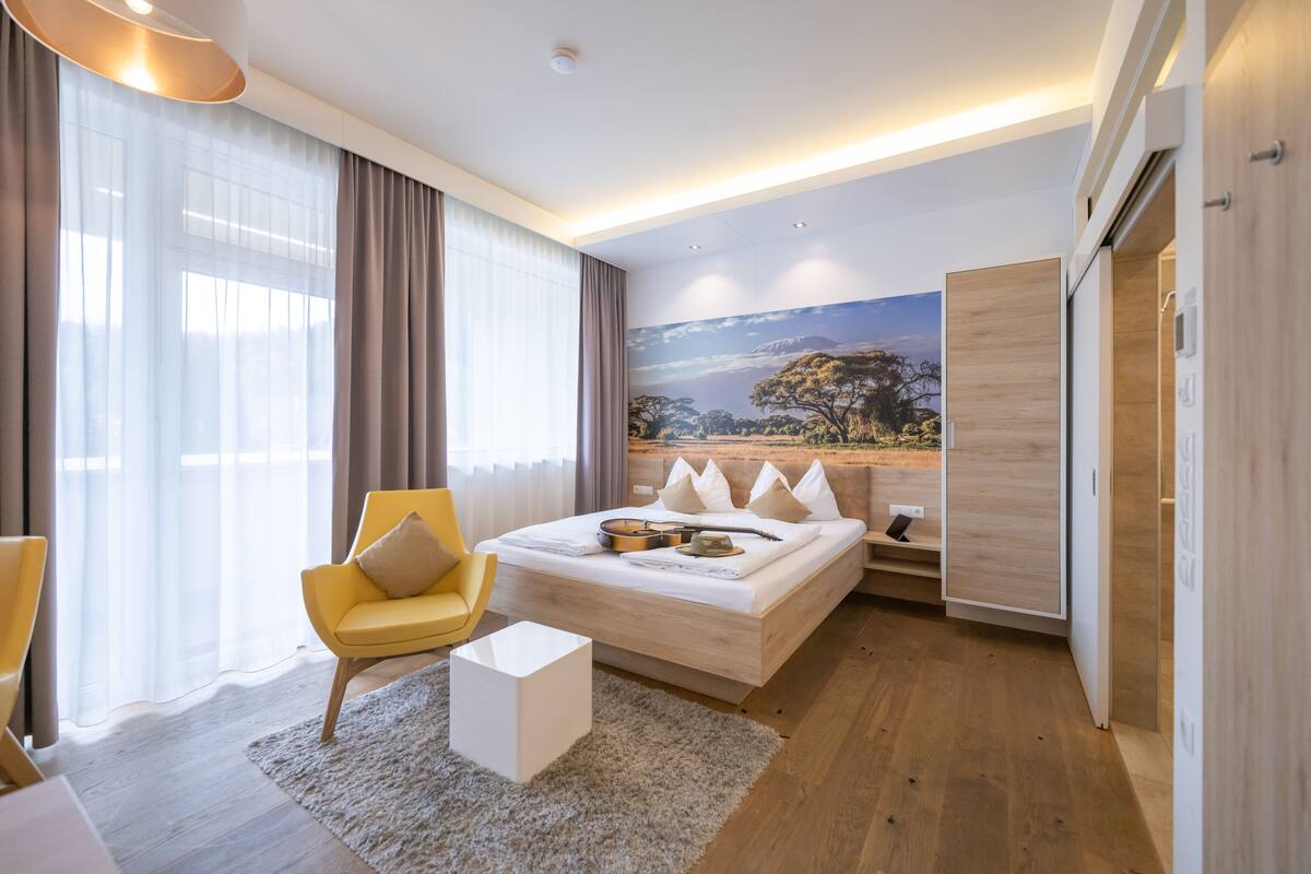 Una habitación de hotel moderna con una cama grande, un sofá, una silla y un cuadro en la pared.