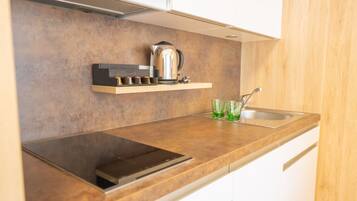 A modern kitchen with a built-in stove, a kettle, and a glass of water on the counter.
