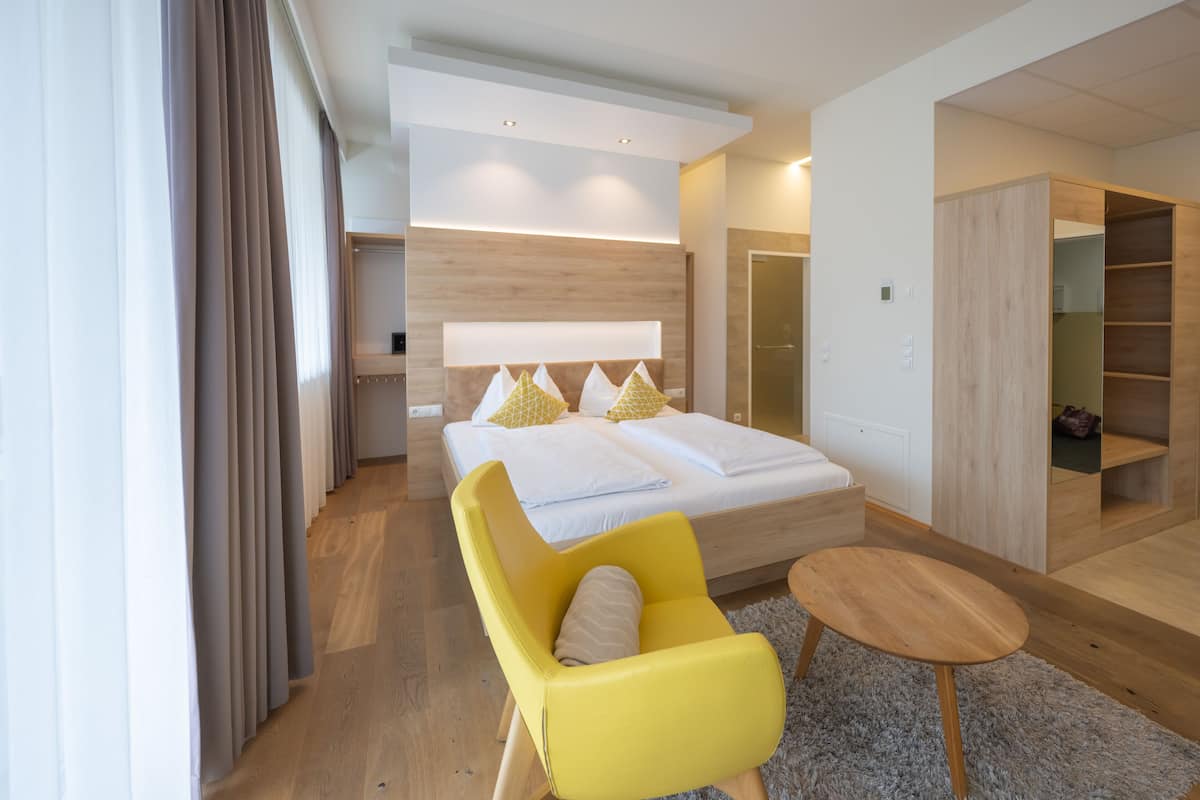 Una habitación de hotel moderna con una cama grande, un sillón amarillo, una mesita de madera y un armario empotrado.