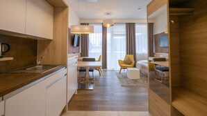 A modern kitchen with a built-in oven, a dining area with a table and chairs, and a living space with a sofa and a TV. - PM PremiumAPART Strassgang (Graz)