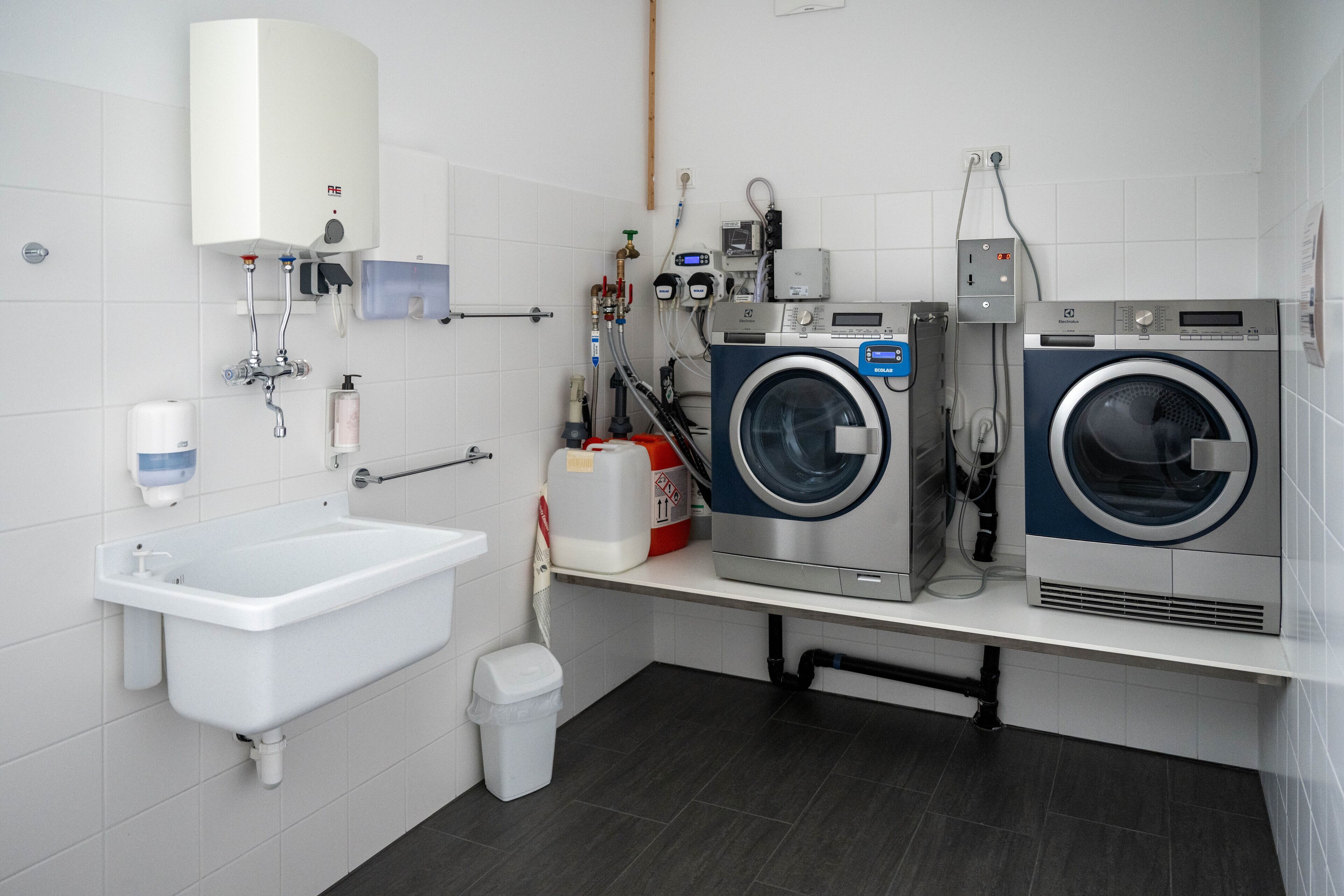 A modern laundry room with two front-loading washing machines, a sink, and a hand dryer.