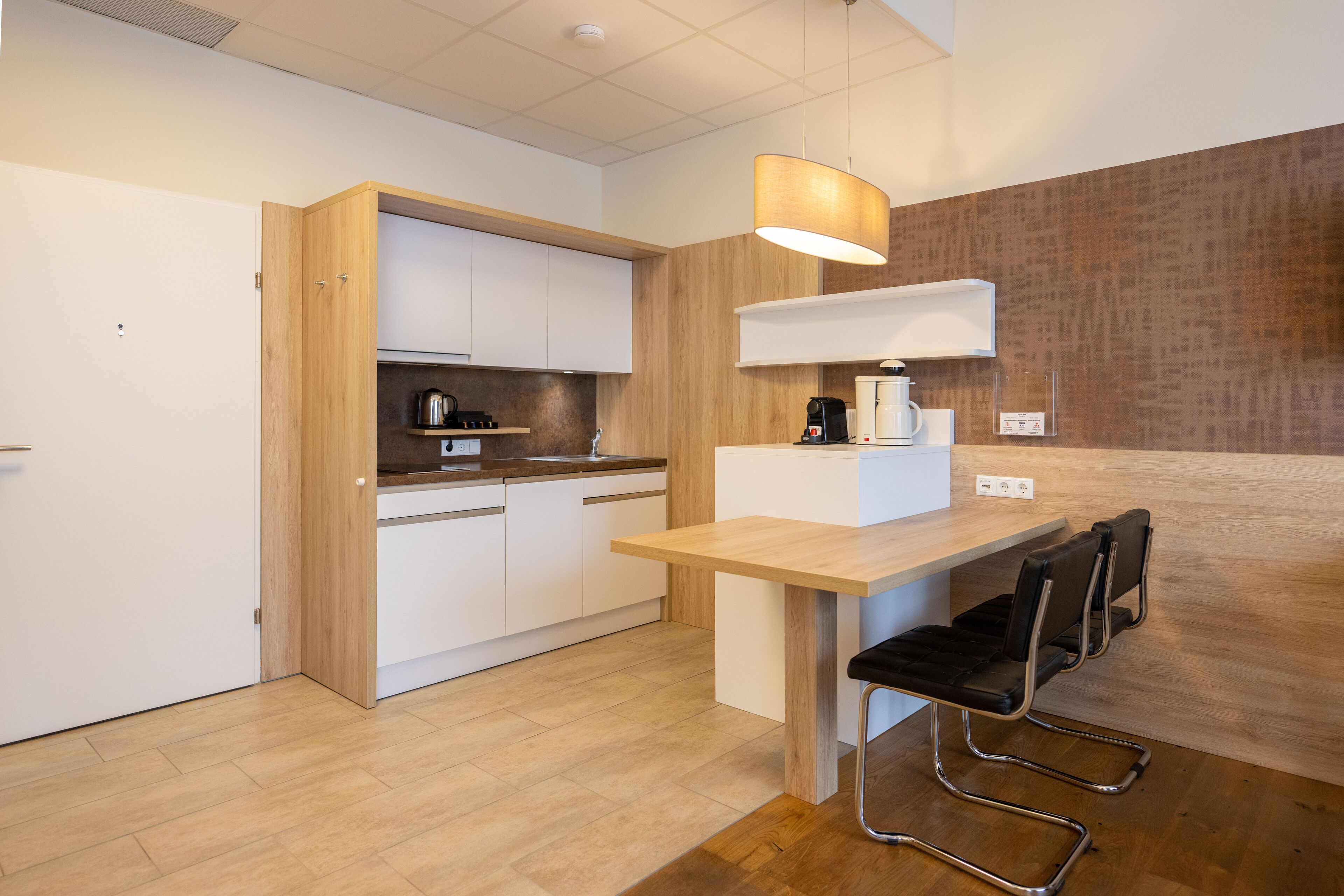Una cocina moderna con armarios blancos, encimera de madera, una cafetera y una mesa con dos sillas.