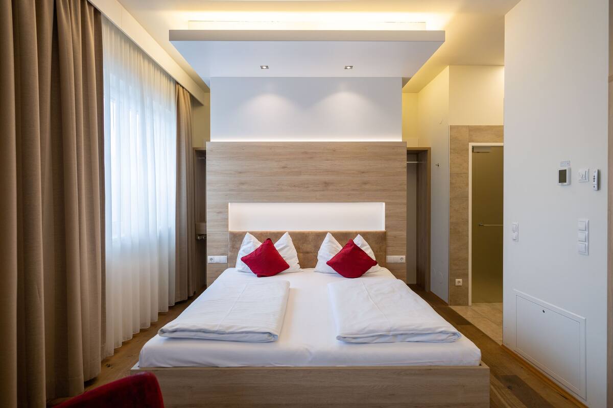 Una habitación de hotel moderna con una cama grande, cabecero de madera y almohadas rojas.