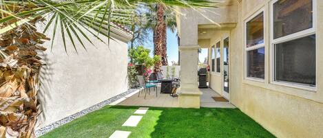 A patio area with a small lawn, a palm tree, and a building with large windows.