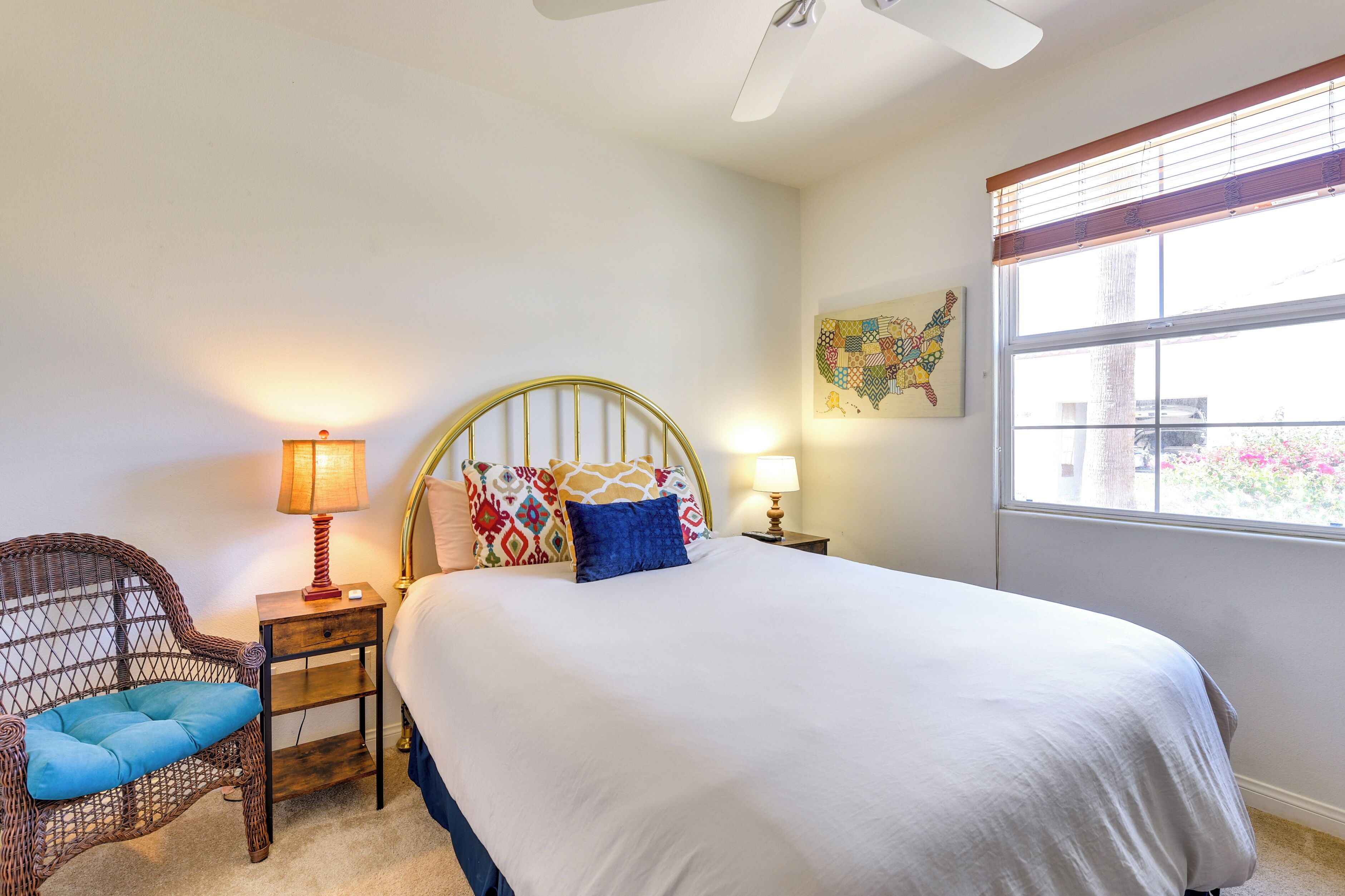 A neatly arranged bedroom with a bed, a chair, a nightstand, and a window with blinds.