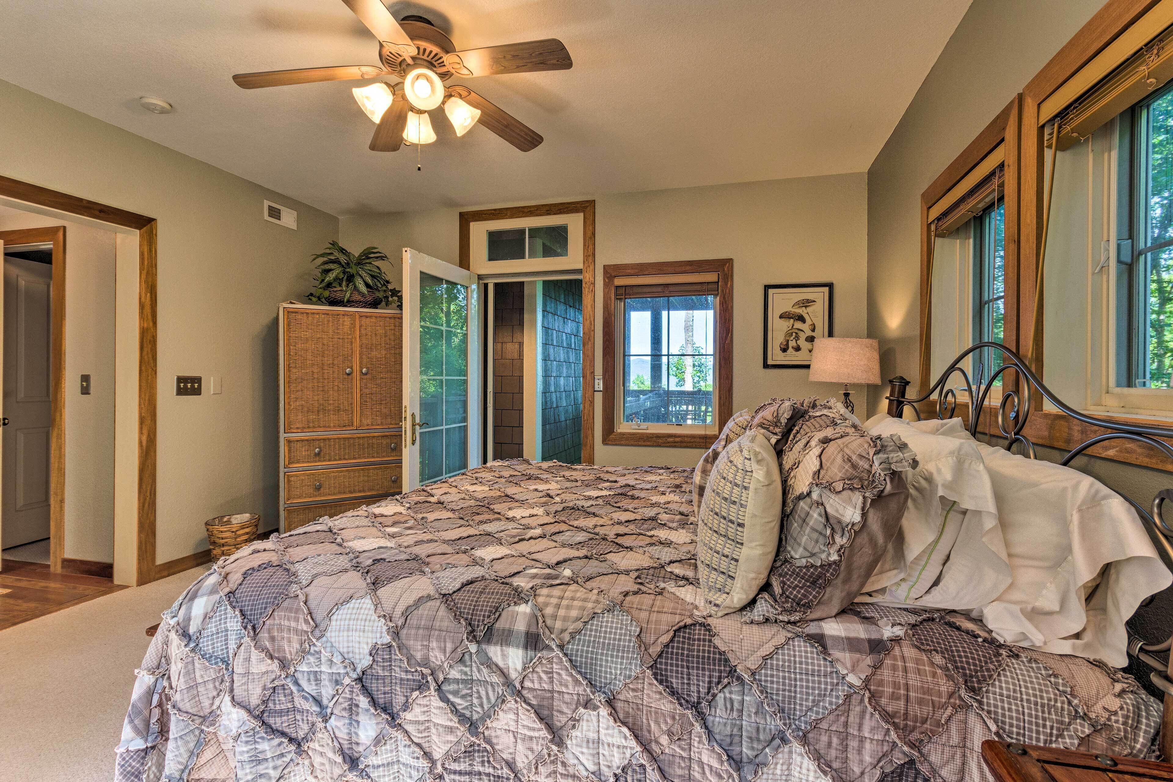 A bedroom with a large bed, a ceiling fan, a wooden wardrobe, and a window with a view of trees.
