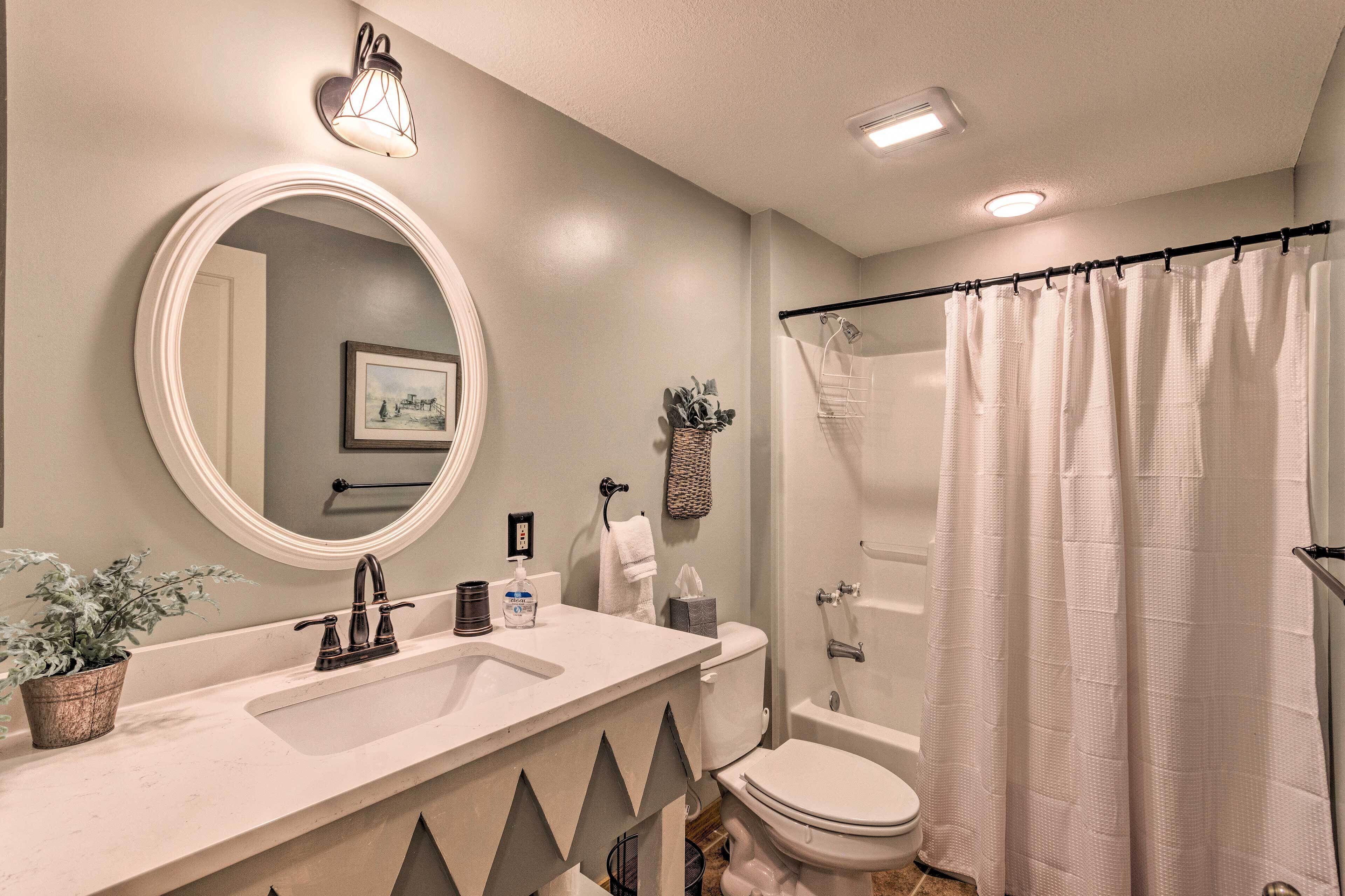 A bathroom with a round mirror, a sink, a toilet, a shower curtain, and a wall-mounted light fixture.
