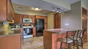 A kitchen with wooden cabinets, a stainless steel refrigerator, a microwave, and a stove. There is a bar area with stools. - Private Dock! Waterfront Group Haven in Camdenton (Camdenton)
