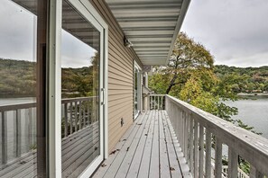 A wooden deck with glass doors leading to a room, overlooking a lake and forested hills.