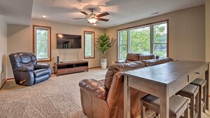 A spacious living room with a leather sofa, a wooden coffee table, a ceiling fan, and large windows offering a view of greenery. - Private Dock! Waterfront Group Haven in Camdenton (Camdenton)