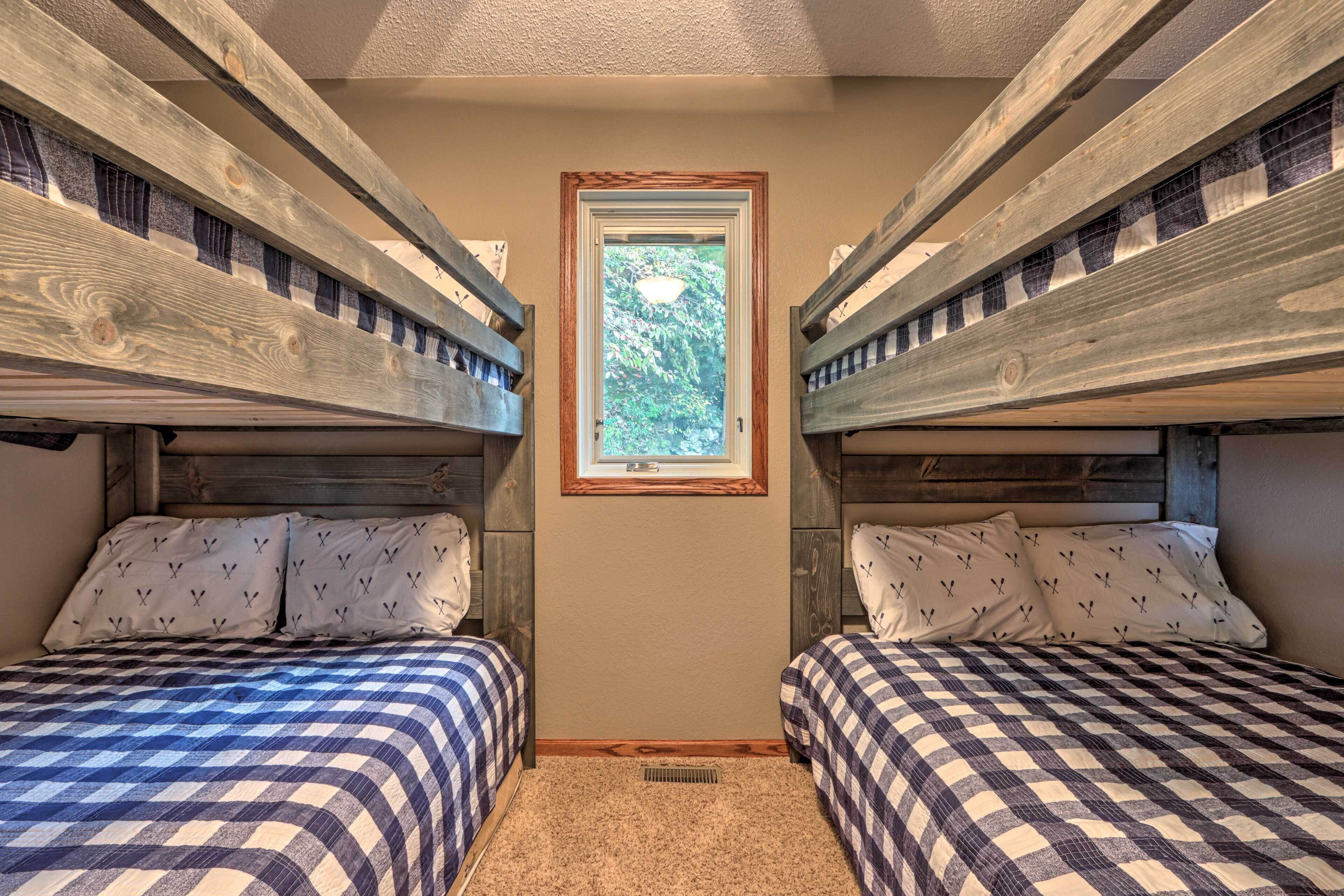 A room with two bunk beds, a window with a view of greenery, and a framed picture on the wall.