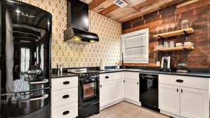 A modern kitchen with a black refrigerator, stove, and dishwasher, white cabinets, and wooden accents on the walls. - The Duet 1 BR- Just Steps from Baylor University and Minutes from The Silos (Waco)