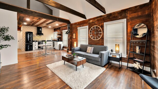 A spacious living area with a grey sofa, wooden flooring, and a large wall clock. - The Duet 1 BR- Just Steps from Baylor University and Minutes from The Silos (Waco)