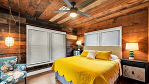 A bedroom with a wooden ceiling, a bed with a yellow bedspread, two bedside tables with lamps, and a floral chair. - The Duet 1 BR- Just Steps from Baylor University and Minutes from The Silos (Waco)