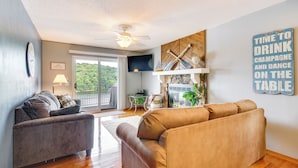 A living room with a brown sofa, a grey sofa, a ceiling fan, a TV, and a sign that reads "TIME TO DRINK CHAMPAGNE AND DANCE ON THE TABLE". - Cozy Lake Ozark Condo Rental w/ Grill, Pool Access (Lake Ozark)