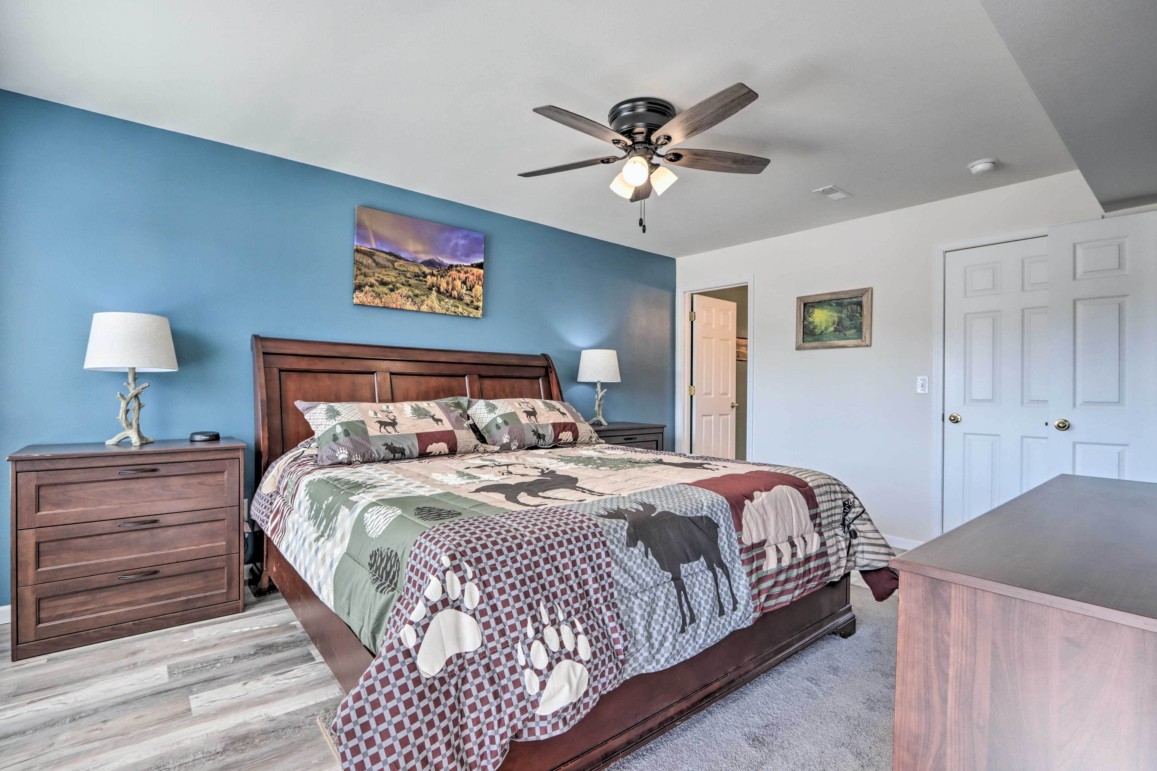 A bedroom with a wooden bed, a ceiling fan, a nightstand with a lamp, and a door.