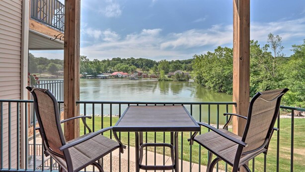 Un espacio exterior cubierto con una mesa y sillas, con vistas a un lago y vegetación circundante.